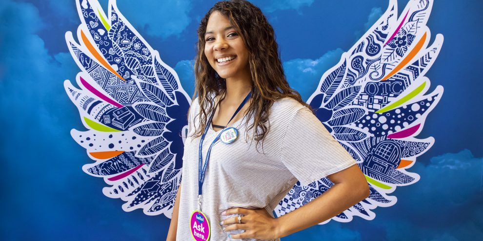 Kaliegha, smiles, and stands confidently in front of the OTC wings backdrop.