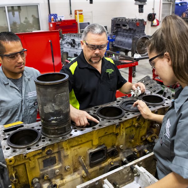 Remanufacturing instructor shows two students a large diesel engine.
