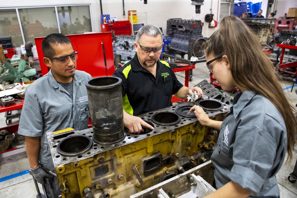 Remanufacturing instructor shows two students a large diesel engine.