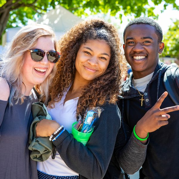 Three students smile and pose at the spring picnic on the plaza.