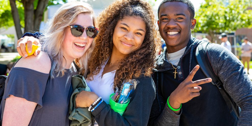 Three students smile and pose at the spring picnic on the plaza.